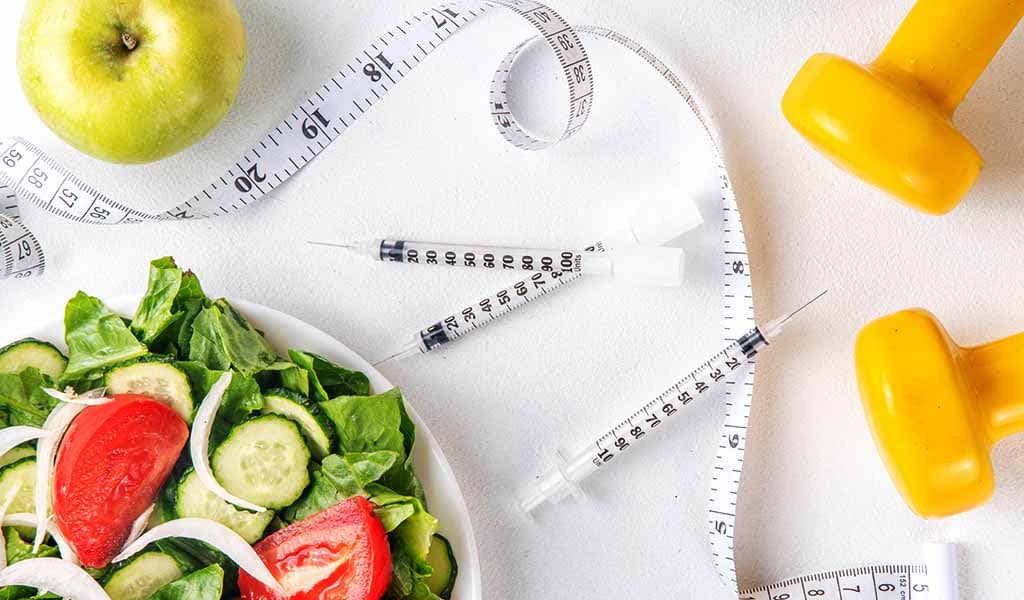 Healthy salad, syringes and dumbbells representing GLP-1 weight loss support at Body Slim Atlanta